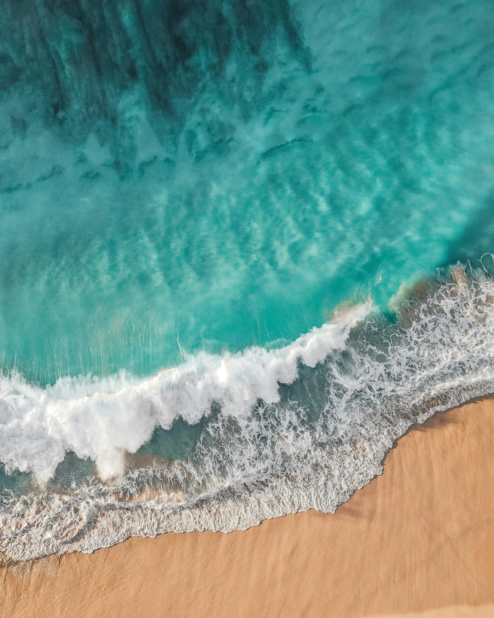 Stunning aerial photo of turquoise waves crashing onto a sandy beach, capturing natural beauty and surf essence.