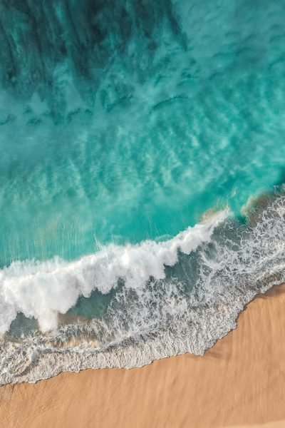 Stunning aerial photo of turquoise waves crashing onto a sandy beach, capturing natural beauty and surf essence.
